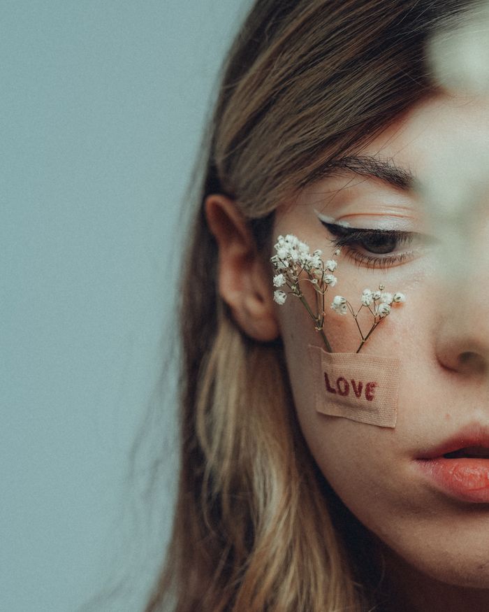 Artistic close-up portrait with delicate flowers and love message on face.